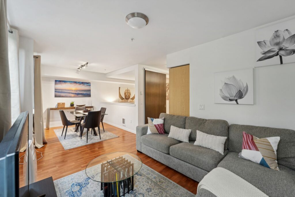 A modern living and dining room area featuring a gray sectional sofa, a glass coffee table, and a dining table with four black chairs.