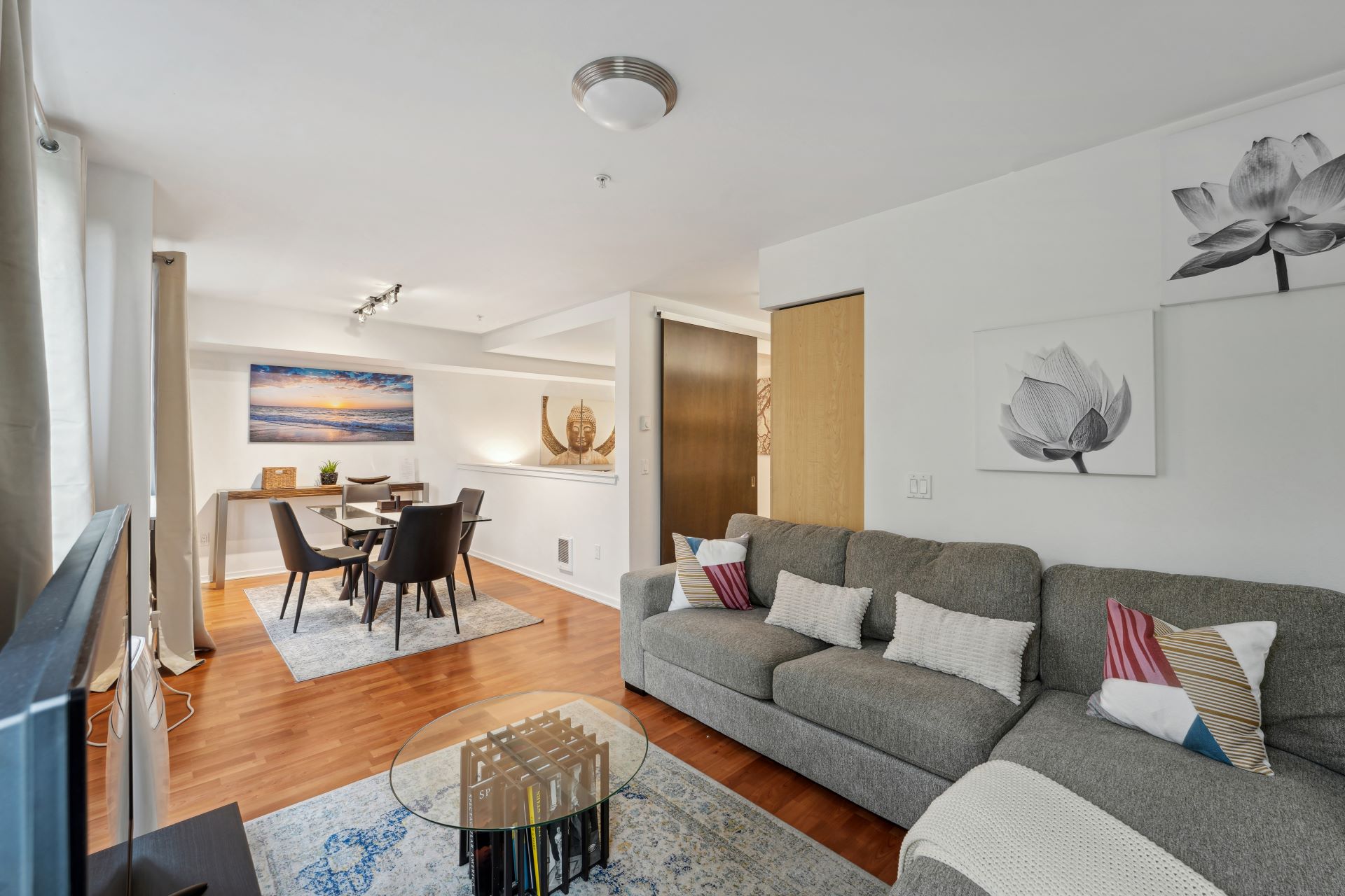 A modern living and dining room area featuring a gray sectional sofa, a glass coffee table, and a dining table with four black chairs.