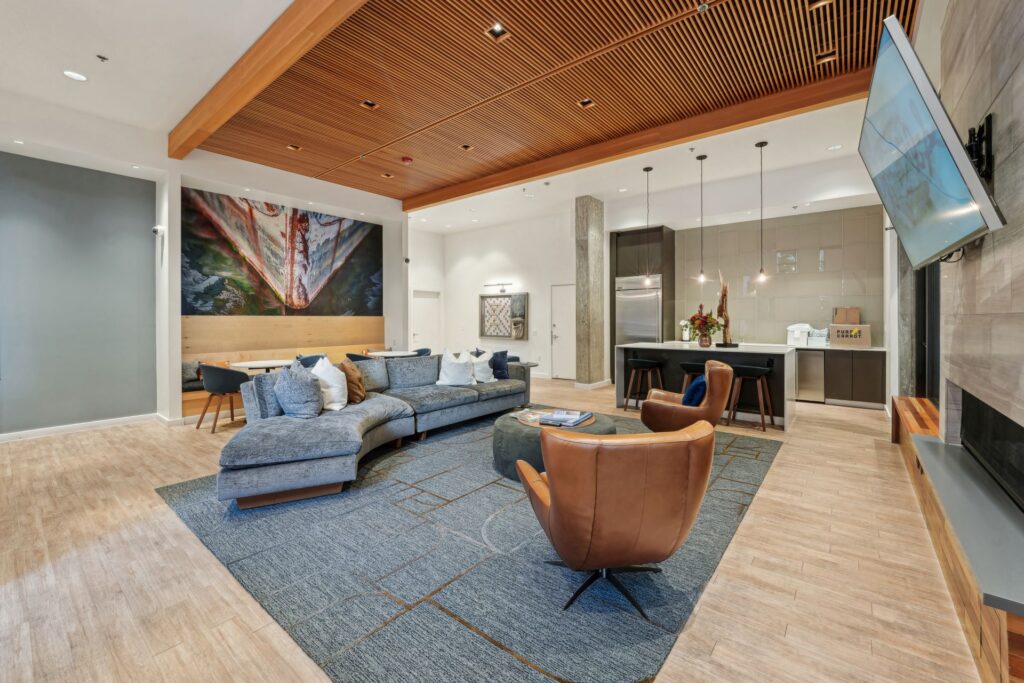 Modern apartment lounge with a curved grey sofa, two leather swivel chairs, a kitchen island with bar stools, and a large wall mural of a ships bow.