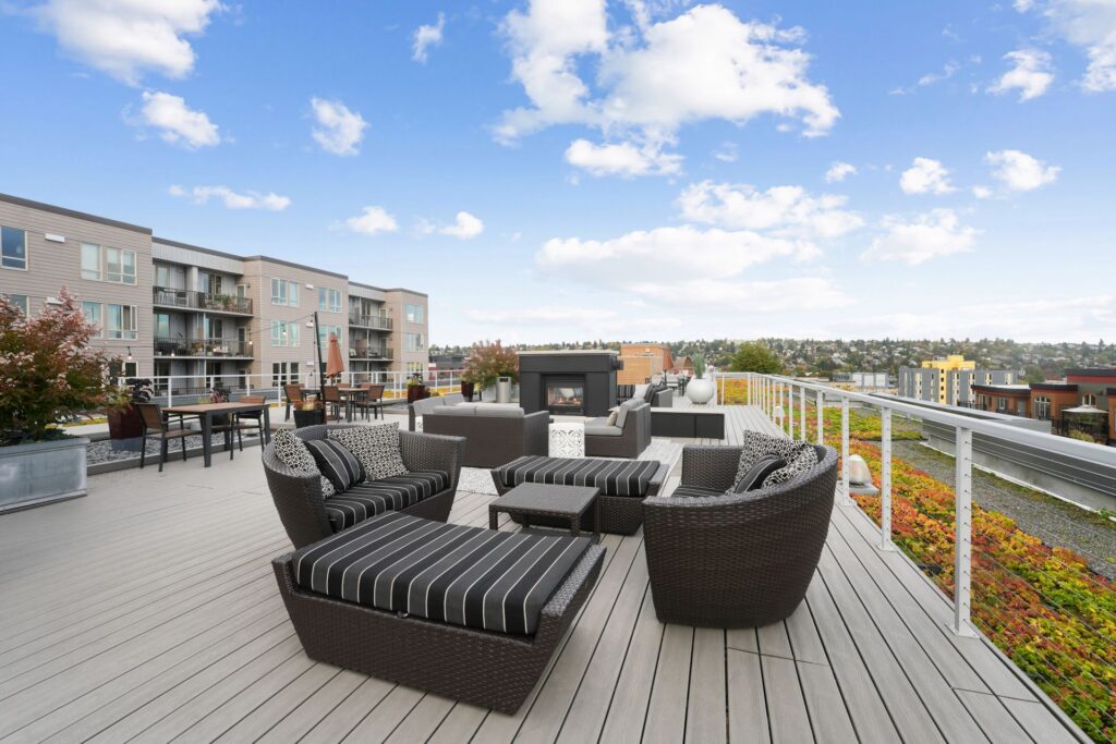 Rooftop terrace featuring multiple seating areas with dark wicker furniture, a central fireplace, and views of a city skyline.