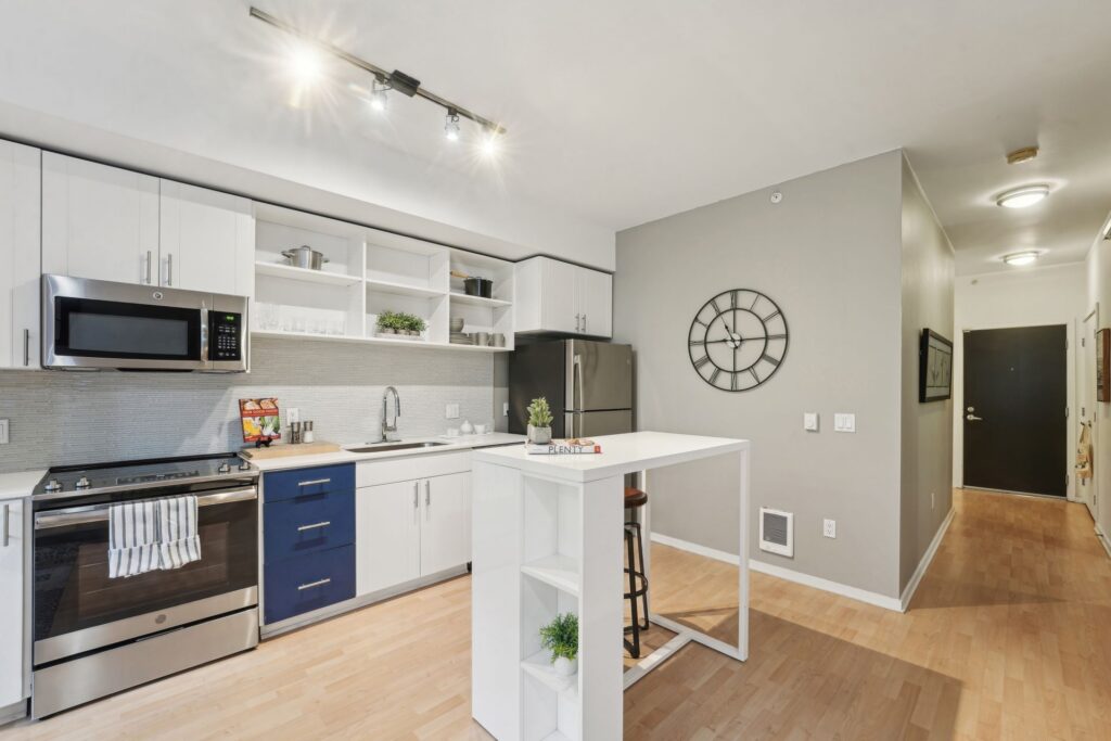 Kitchen with white cabinets, blue lower drawers, stainless steel appliances, and a central white island with a stool.