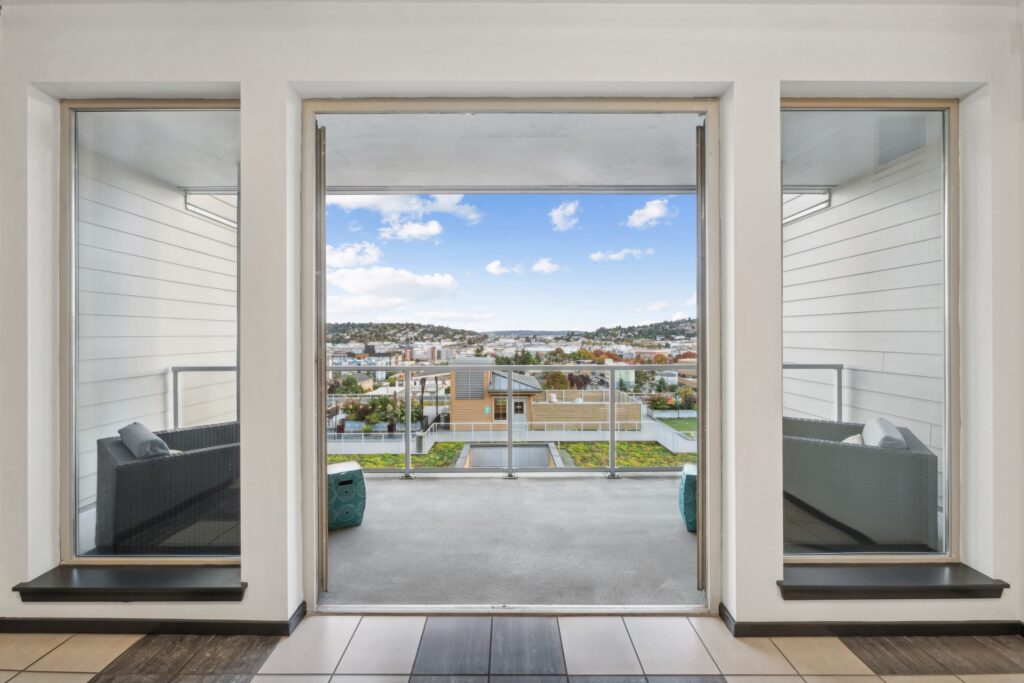 View through a doorway leading to a balcony overlooking a city skyline and a green roof.