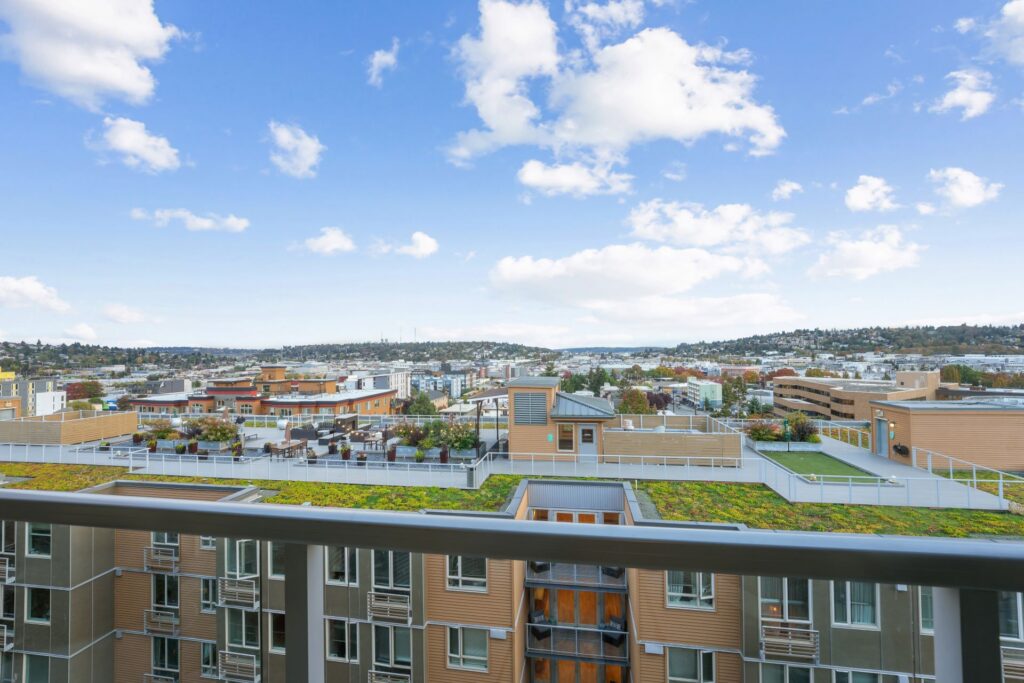 View from a high-rise balcony looking out over a city skyline and neighboring buildings with green roofs.