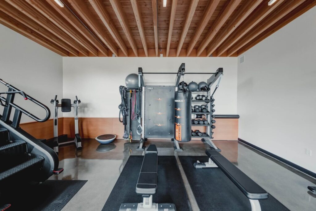 A gym space featuring a central Torque fitness rack with an attached punching bag, weight storage, and resistance bands, flanked by two weight benches, a stair climber, and a balance ball.