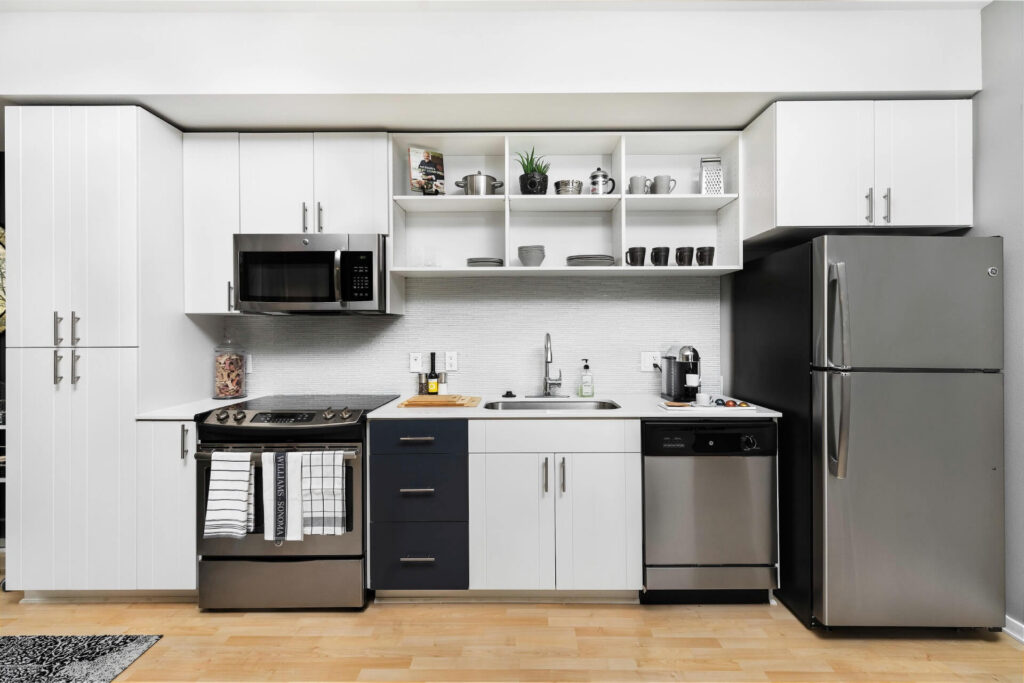 Modern kitchen with white and dark blue cabinetry, stainless steel appliances, and open shelving above the sink.