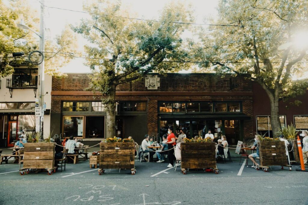 Outdoor dining area with tables set up in a street parking lane in front of a brick restaurant building.